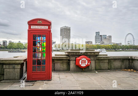 Old style London Telephone box with stained glass on the back panel with the London Eye in the distance and river thames and in London, England Stock Photo
