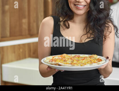 Selective focus of delicious pizza in hands of female client in cafe. Attractive long haired brunette eating and enjoying tasty food in pizzeria. Concept of fast food and gastronomy. Stock Photo