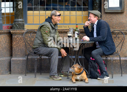 London, UK. Two men and a dog outside the Clarence pub in Whitehall. One drinking beer, the other wine Stock Photo