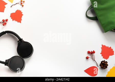Wireless headphones black and green backpack bag branches red leaves berries on white background. The concept of autumn. Modern technology. Top view f Stock Photo
