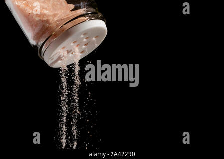 Pink himalayan salt falling out from a salt shaker on a black isolated background Stock Photo