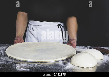 Chef holding uncooked pizza with on table in black background. Stock Photo