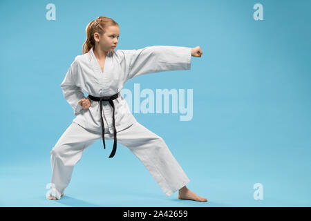 Pretty, young girl practicing karate and jujitsu. Confident junior wearing in white kimono with black belt standing in stance. Concept of wellness and martial arts. Stock Photo