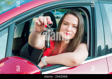 Focused car shaped keychain with keys on the background of happy successful woman sitting in her new car. Outdoors view. Selective focus, copy space Stock Photo