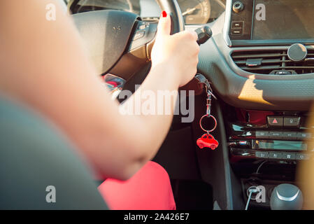 Car key in ignition. Start, stop or accelerate engine. Car shape keyfob on vehicle dashboard background during driving. Woman driver. Selective focus, Stock Photo