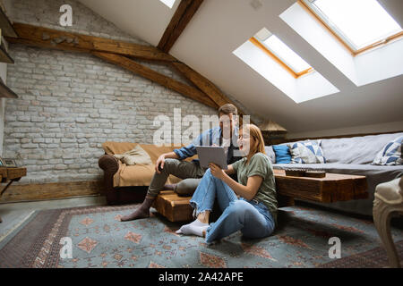 Happy young couple using tablet sitting on the floor at home