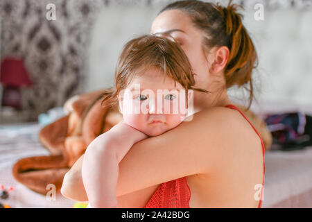 baby is happy in mom's arms. smiling mom. joyfully spending together. home furnishings. when dad is at work Stock Photo