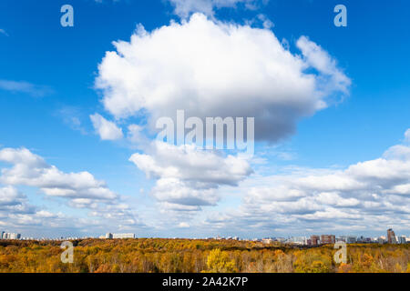 wedge of cumuli clouds in blue sky over yellow forest and city on sunny autumn day Stock Photo