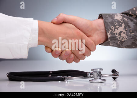 Doctor And A Military Man Shaking Hands Over The Stethoscope On White Table Stock Photo