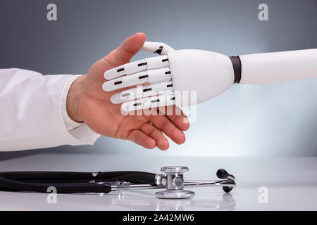 Doctor And Robot Shaking Hands Over Stethoscope Stock Photo