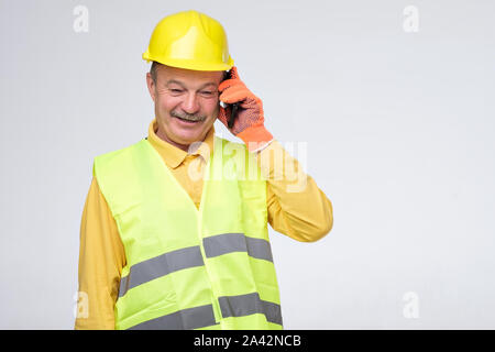 Repairman in protective helmet talking on his phone with client Stock Photo