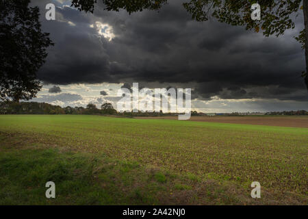 A wide view over a harvested field under a dramatic, dark sky. Stock Photo