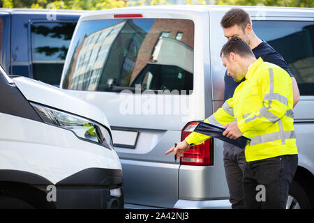 Insurance Agent Examining Car After Accident Claim Being Assessed And Processed By Man On Street Stock Photo