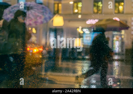 Rain on a window, looking out to people in a night street scene. Silhouettes of people with umbrellas