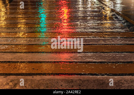 Pedestrian crossing in rainy evening. Road markings on asphalt with bright reflected from traffic lights. Striped yellow background and texture Stock Photo