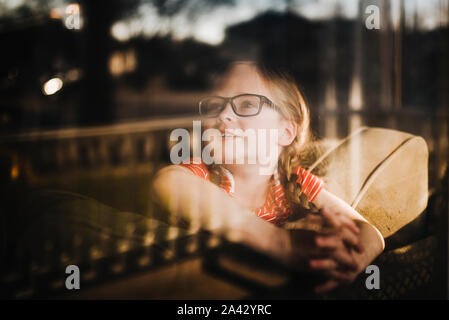 Front view of little girl looking out of window with reflections Stock Photo