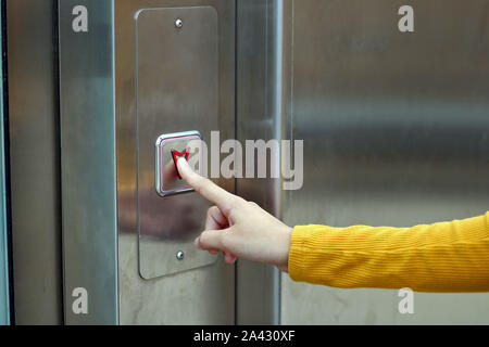 Girl dressed in yellow biting the elevator button. Elevator to access the metro. Stock Photo