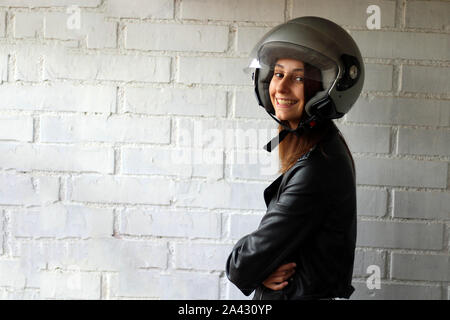 Girl dressed in a leather jacket and with a grey motorcycle helmet. Stock Photo