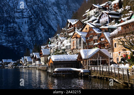 Traditional wooden lakeside houses of Hallstatt town with snow on the roofs with Alps mountains in the background in winter in Gmunden, Upper Austria. Stock Photo