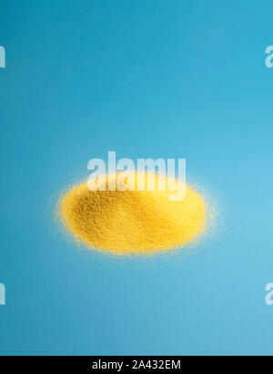 Golden corn flour pile on a blue paper background. Freshly grounded maize. Cooking ingredient for polenta and cornbread. Raw corn products. Stock Photo