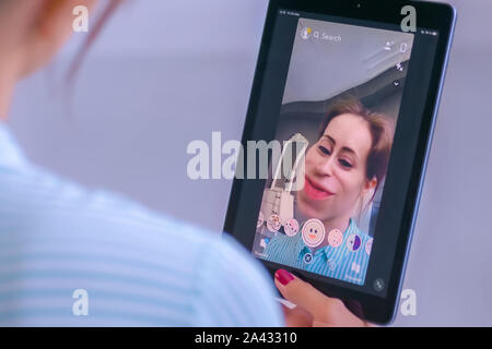 Woman using Snapchat multimedia messaging app with face mask on tablet Stock Photo