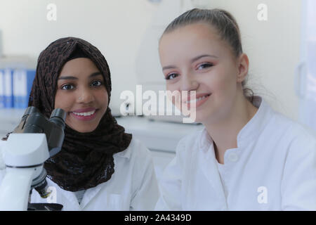 Two young female multiethnic scientists looking at camera and smilling ...