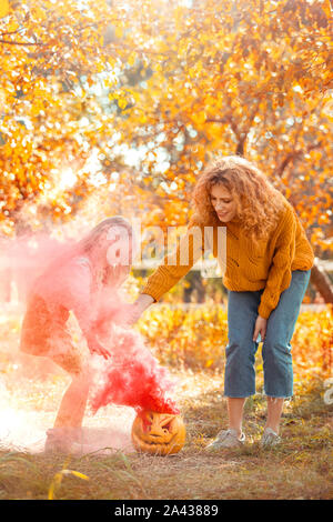 Halloween Preparaton Concept. Mother and daughter standing outdoors making colored gas in pumpkin joyful Stock Photo