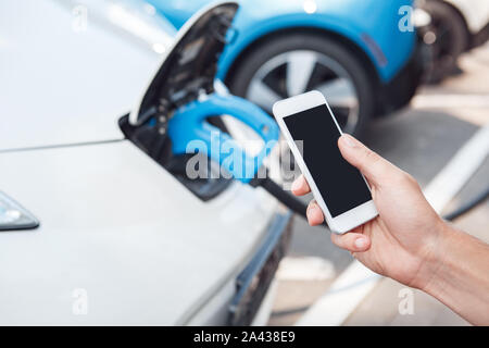Young adult man using smartphone and paying for charging electric car Stock Photo