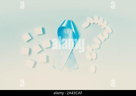 Sugar cubes, Diabetes Awareness Blue Ribbon, blood test, and question made of pills on plain blue background. World Diabetes Day concept, toned Stock Photo