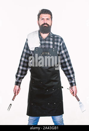 Being ready for bbq party. Grill cook holding spatula and bbq fork. Bearded man with bbq tools in hands. Happy hipster using stainless steel tools for preparing bbq food. Stock Photo