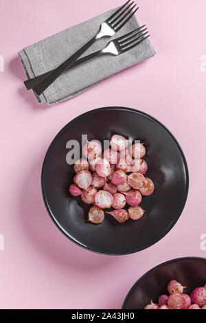 Beautiful roasted radishes in a black plate on pink table close up. Stock Photo