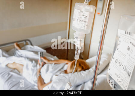 Valencia, Spain - September 10, 2019: Saline solution drip  bag hanging on the bed of a sick woman. Stock Photo