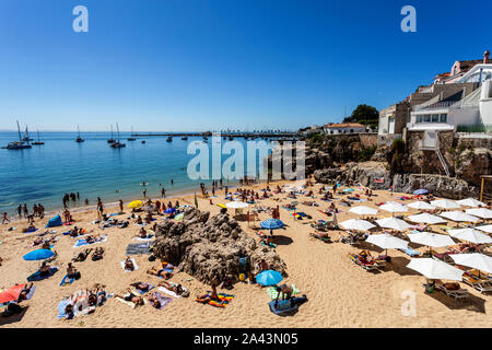 View of the crowded pretty little beach named Praia da Rainha along the beach promenade between the towns of Estoril and Cascais, nearby Lisbon, Portu Stock Photo