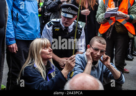 London, UK. 8th Oct, 2019. A police officer tries to inform two sitting protesters that they will be arrested if they do not move during the demonstration.Thousands of protesters take to the streets in London calling on the UK government to tackle climate change in what they are calling ''˜Rebellion Week'. Causing mass disruption in central London by blocking roads and disturbing the usual workings of government. Boris Johnson, the British Prime Minister, responded to the protest with anger and frustration. At an event in London on Monday, Mr. Johnson referred to the demonstra Stock Photo