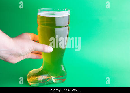 A hand holding a beer boot glass in green background Stock Photo
