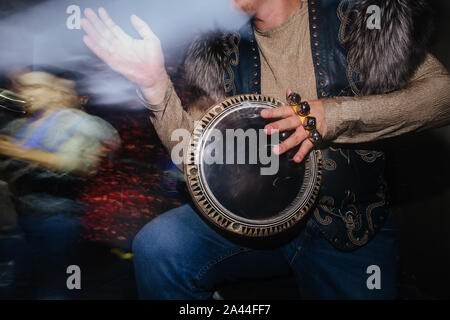 Close up of musician in extravagant native clothes plaing on hand drum. Stock Photo