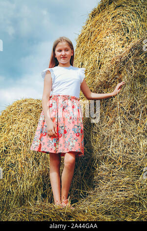 a schoolgirl with long hair in a pink dress climbed on large bales of straw on a hot summer day 2a44gaa
