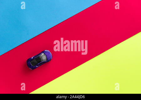 Kids toy car on trendy colorful background. Baby car top view on blue red yellow colored paper. Boys game. Travel and sport lifestyle. Business, transportation concept. Moscow, Russia - September 30, 2019 Stock Photo