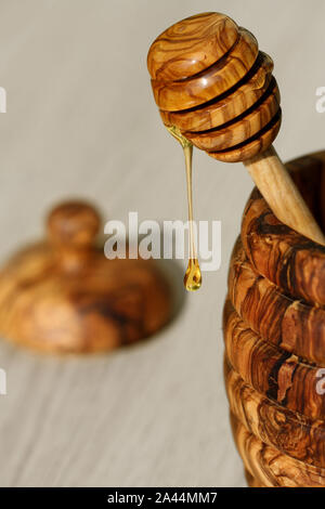 honey dripping from a wooden honey dipper with olive wood honey jar Stock Photo