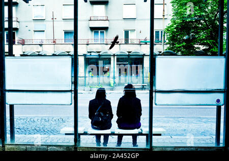 two young women sitting at a bus stop Stock Photo