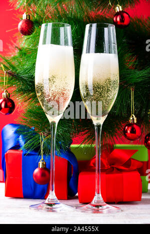 Two glasses for champagne, a red Christmas ball hanging on a spruce branch, gifts with multi-colored blurred lights, a card for New Year's greetings Stock Photo
