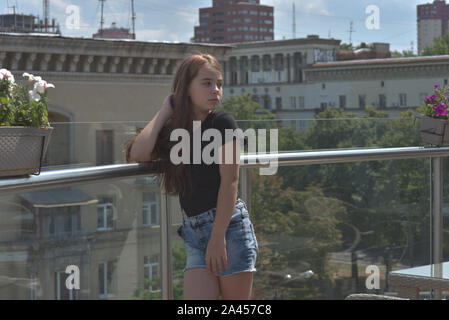 Young European teenage brunette curly model posing.Teenager girl in a black T-shirt. Girl 10 years old posing on the veranda in a cafe or on the balco Stock Photo