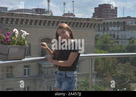 Young European teenage brunette curly model posing.Teenager girl in a black T-shirt. Girl 10 years old posing on the veranda in a cafe or on the balco Stock Photo