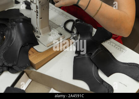Sewing machine in a leather workshop in action with hands working on a leather details for shoes. Women's hands with sewing machine at shoes factory Stock Photo