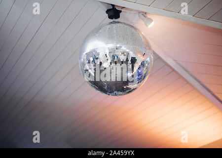 Spheric disco ball on the ceiling.Close-up of silver shining disco ball fixed on the white wooden ceiling at the party. Stock Photo