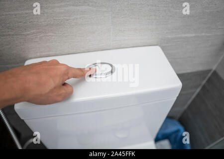 Close up of finger pushing a flush toilet button for cleaning a toilet. Stock Photo