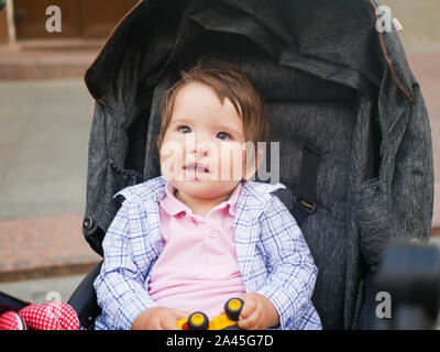 Baby sitting in a gray stroller. holding a toy in the hands. A warm walk for the baby. Stock Photo