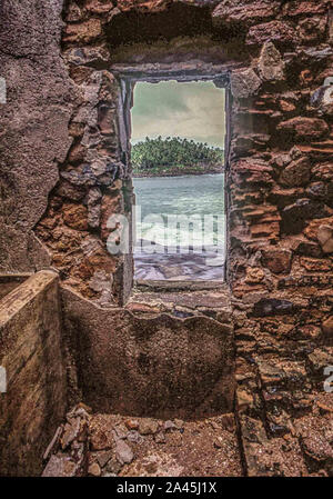 October 11, 2019, Devil'S Island, French Guiana: Through ruins a view of the rocky islet of Devils Island (Isle du Diable) from Isle Royale, one of the three islands (Royale, Saint-Joseph, and Diable) of the volcanic Isles du Salut group off French Guiana, collectively called Devils Island (Isle du Diable). Now a nature reserve, serving tourists and cruise ship passengers, visitors are not allowed on small Devils Island but tour the decaying old prison facilities on nearby Isle Royale. (Credit Image: © Arnold Drapkin/ZUMA Wire) Stock Photo