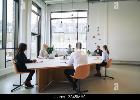 Smiling group of diverse work colleagues discussing business together while sitting around a boardroom table in an office Stock Photo