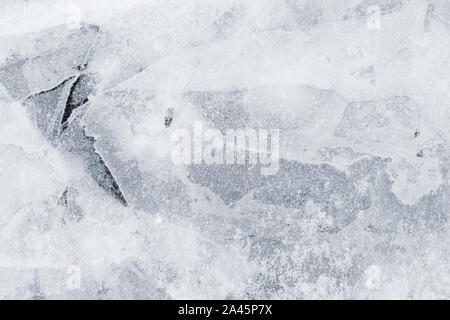 Close-up of snow on cracked and thin layers of ice in the winter. Simple and minimal full frame abstract background in black and white. Copy space. Stock Photo